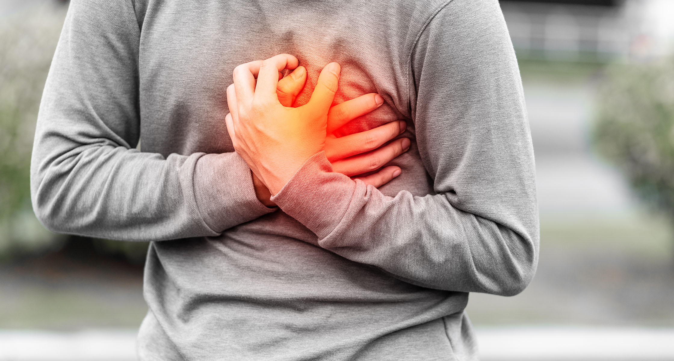 A person in a gray sweatshirt clutches their chest, experiencing pain, with a glow indicating discomfort surrounding their hands.