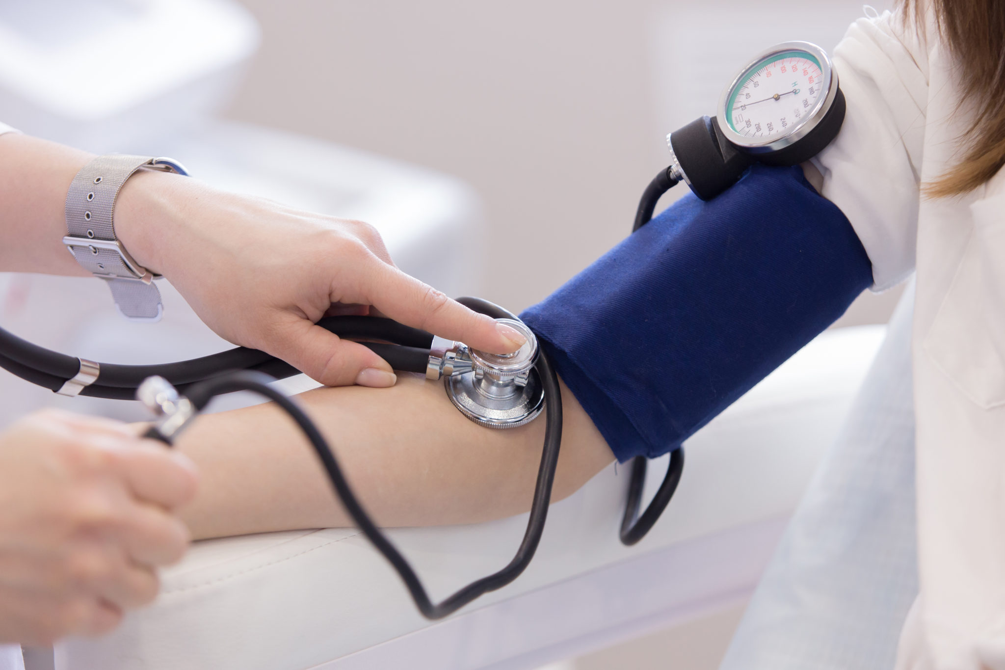 A healthcare professional measures high blood pressure using a blue cuff and stethoscope. The setting is clinical, conveying a sense of care and precision.