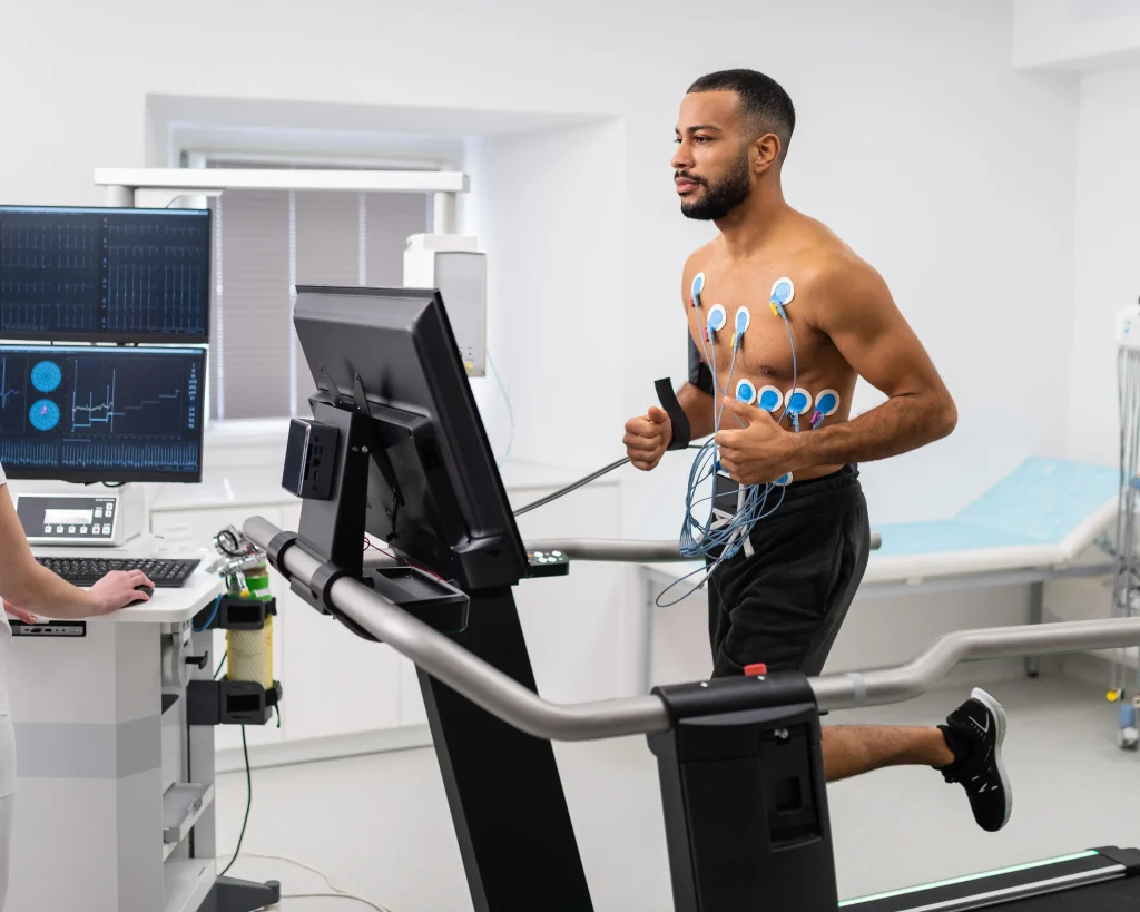 A man running on a treadmill during a cardiac stress test in a medical clinic, monitored by a technician as part of Heart Checkup Packages in Dubai.