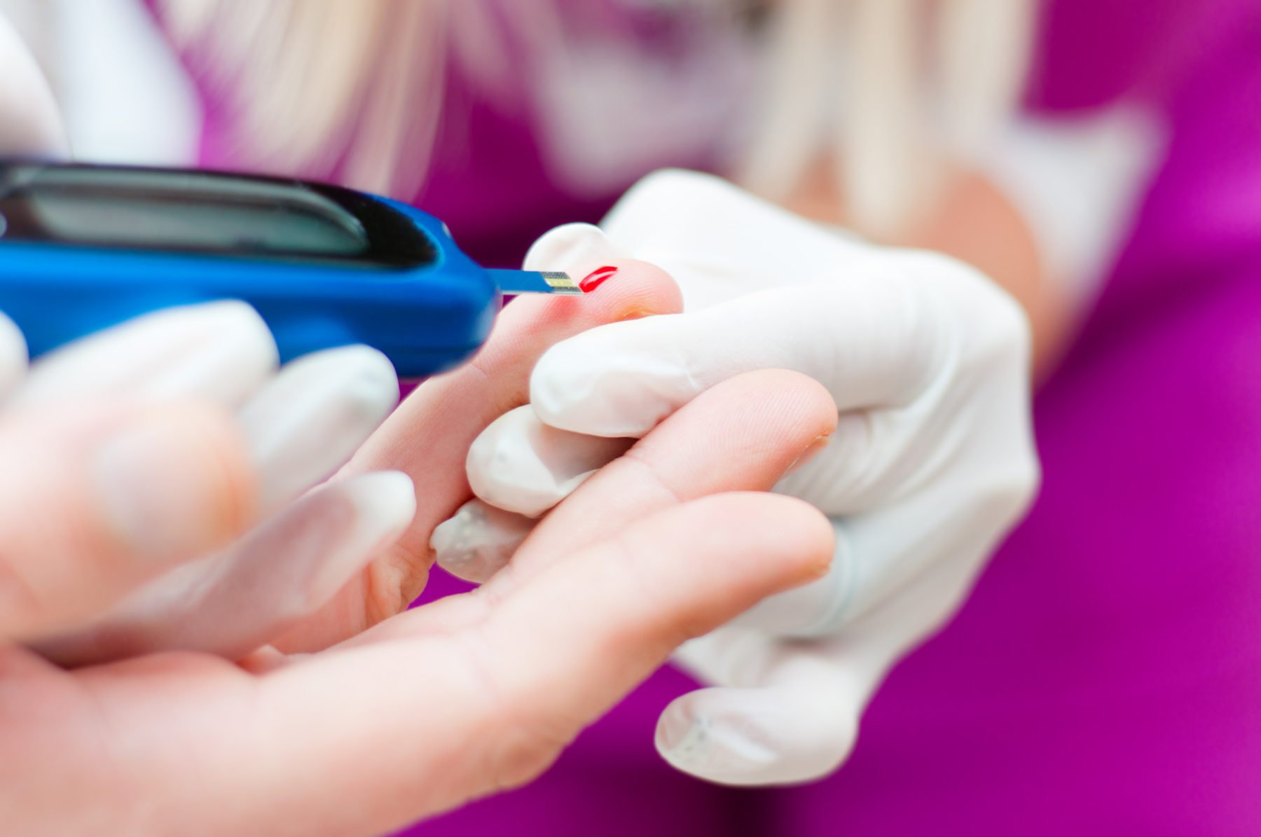 A gloved hand holds a finger while a glucose meter tests a drop of blood, symbolizing Diabetes and heart disease monitoring, precision, and professional medical care.